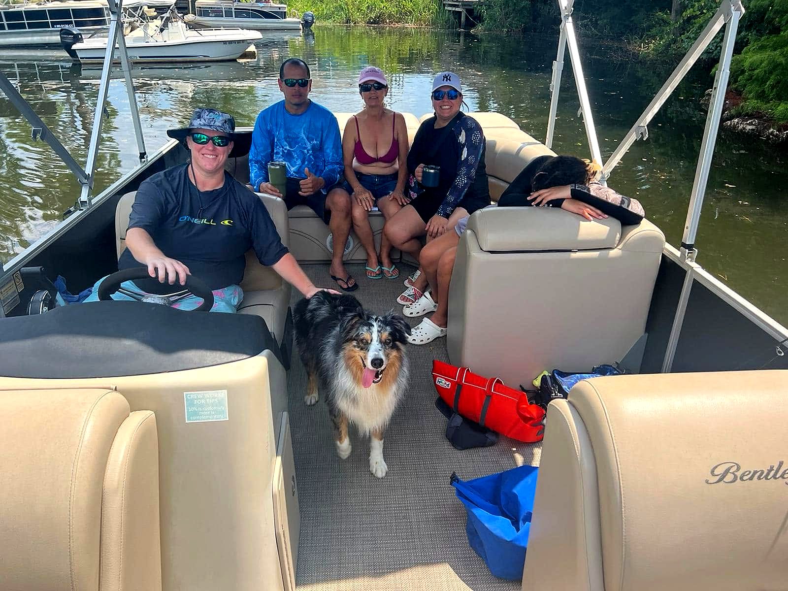 A group of friends and a dog relaxing on a pontoon boat with Hollie at the helm