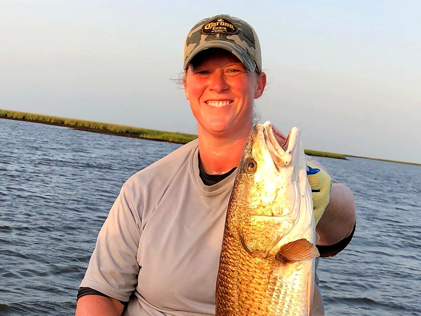 Hollie smiling on the boat holding up a big redfish in the marsh