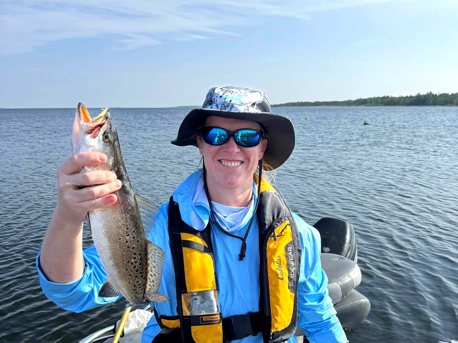 Hollie in a life vest holding a speckled trout on the water