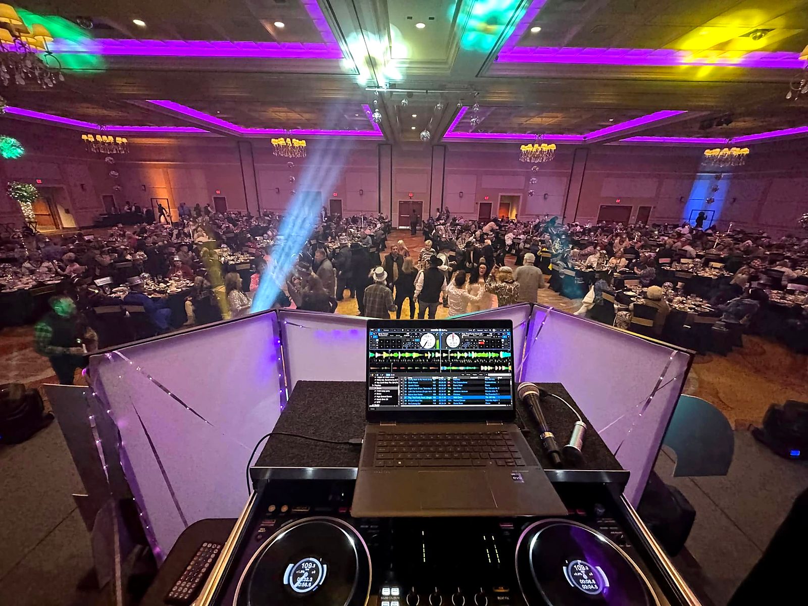 View from Hollie's DJ booth over a packed ballroom dance floor with purple LED uplighting and moving lights