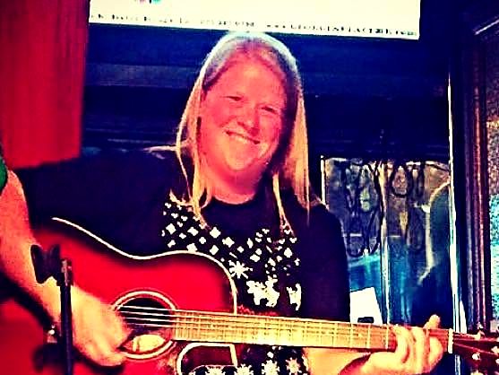 Hollie smiling and playing a red acoustic guitar