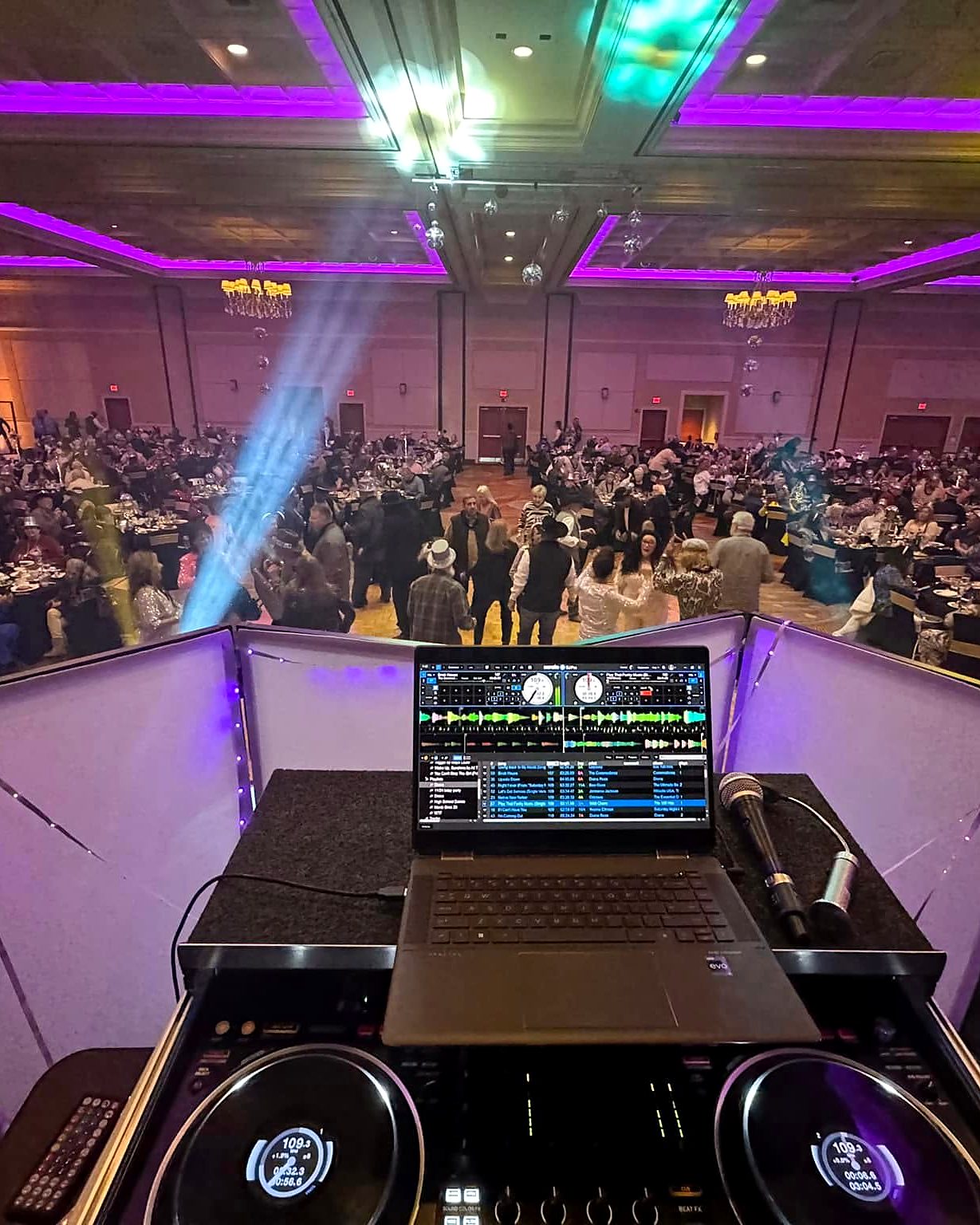 View from Hollie's DJ booth: turntables and laptop in front of a ballroom dance floor washed in purple LED uplighting and moving light beams